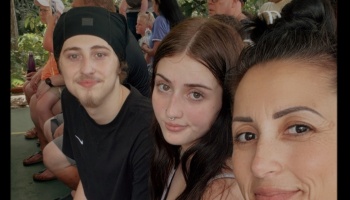 A woman takes a selfie with a young man wearing a black beanie and a young woman with dark hair.