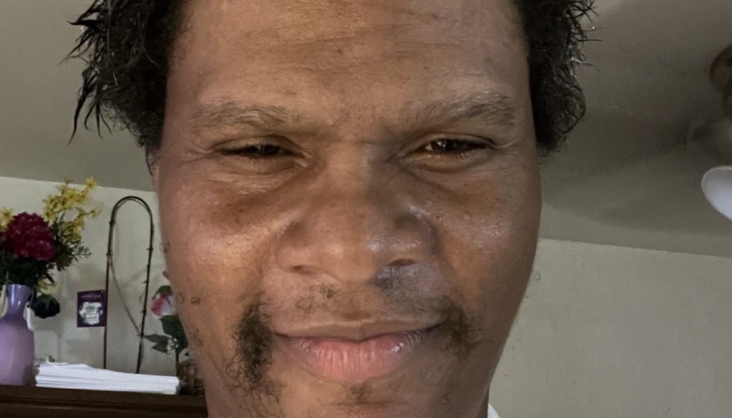 Close-up selfie of a smiling man with dark curly hair and a thin mustache looking into the camera.