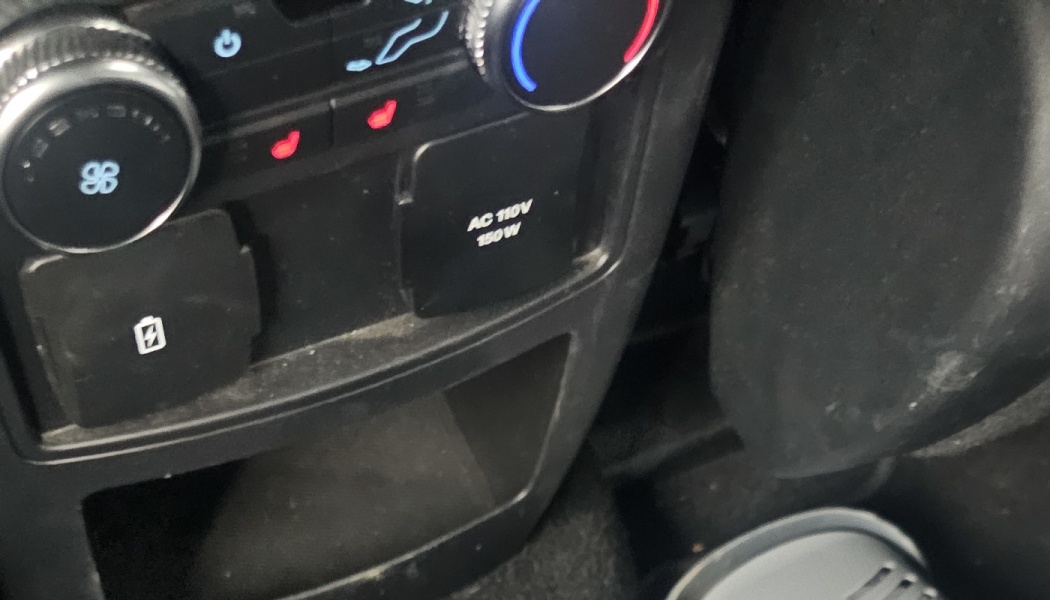 Vehicle console featuring climate dials, heated seat controls, a charging port, and an AC 110V 150W power outlet.
