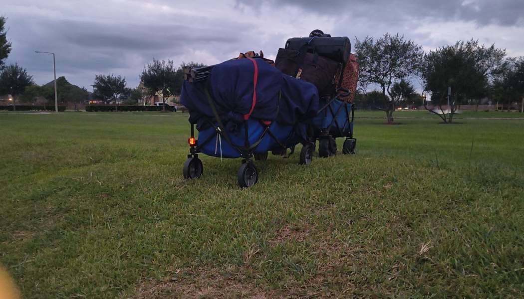 Two utility wagons heavily loaded with bags and gear parked on a grassy field under a cloudy sky.