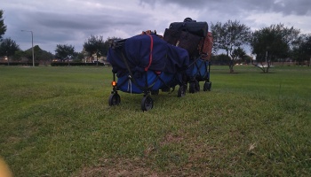 Two utility wagons heavily loaded with bags and gear parked on a grassy field under a cloudy sky.