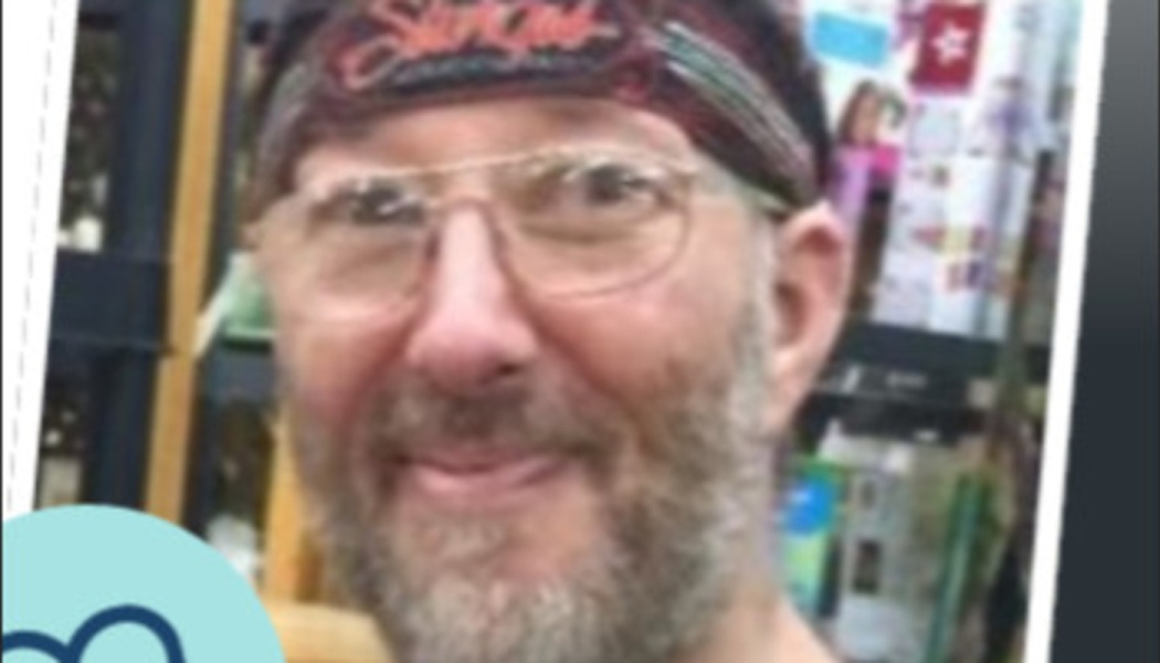 Smiling man with a beard, clear glasses, and a patterned headband.