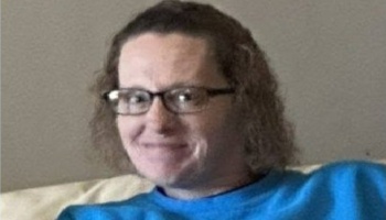 Smiling person with glasses and curly hair wearing a bright blue shirt.