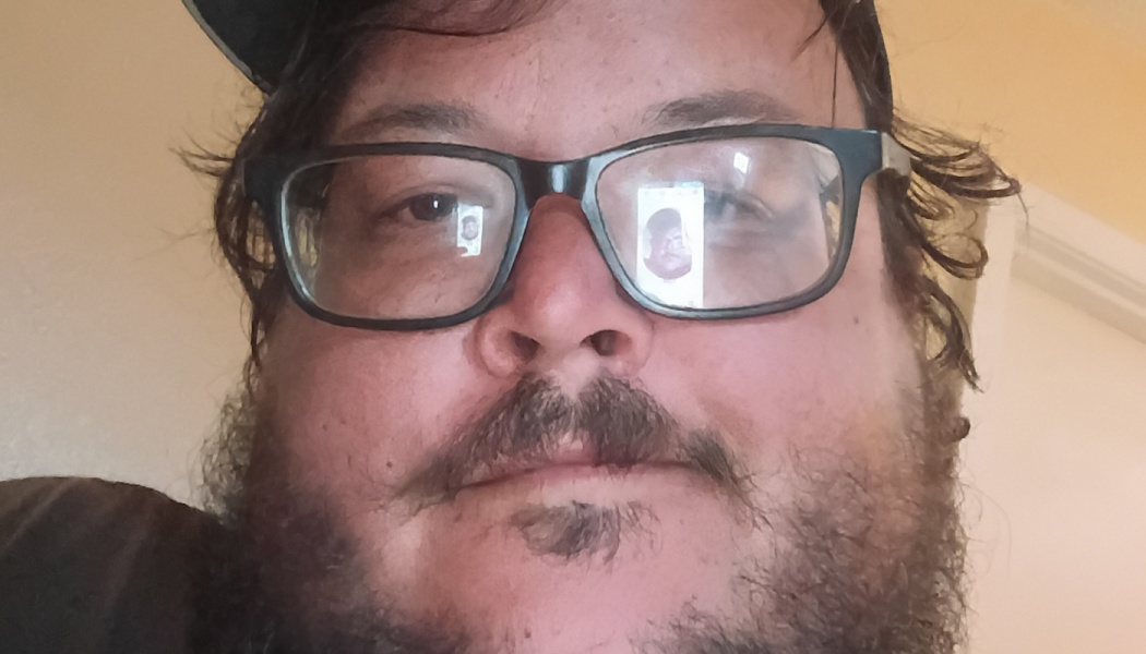 Close-up selfie of a bearded man wearing black-framed glasses and a cap.