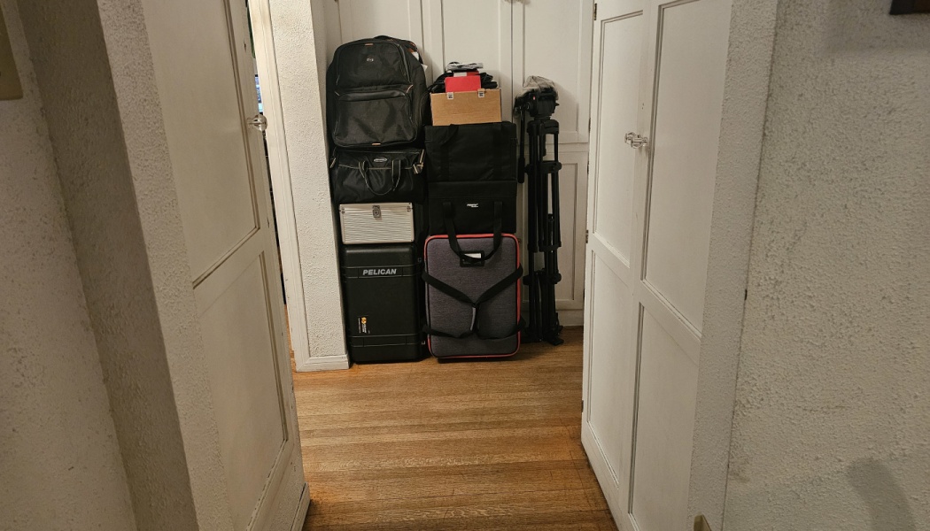 Camera gear, hard Pelican cases, backpacks, and a tripod stacked neatly in a room alcove.