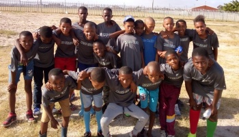 A group of smiling young boys in matching grey shirts posing together on an outdoor field.
