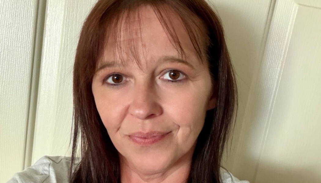 Close-up portrait of a woman with dark brown hair and bangs smiling gently at the camera.