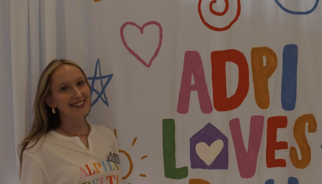 Smiling young woman standing beside a colorful hand-painted banner that reads "ADPi LOVES."