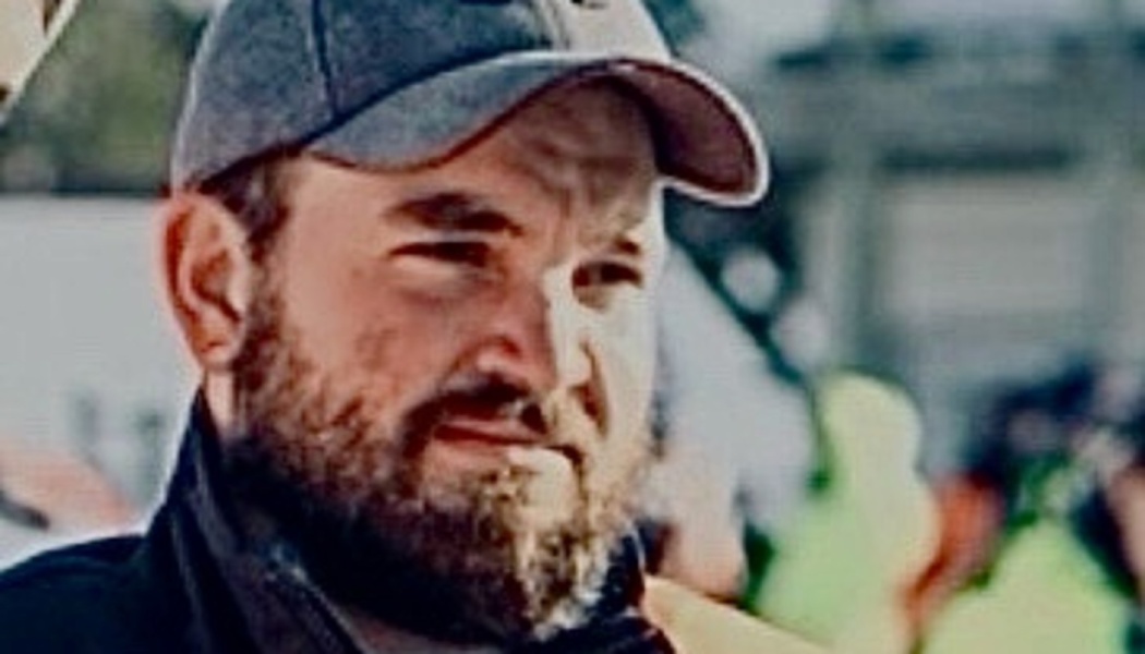 Close-up of a bearded man wearing a grey baseball cap looking off to the side.