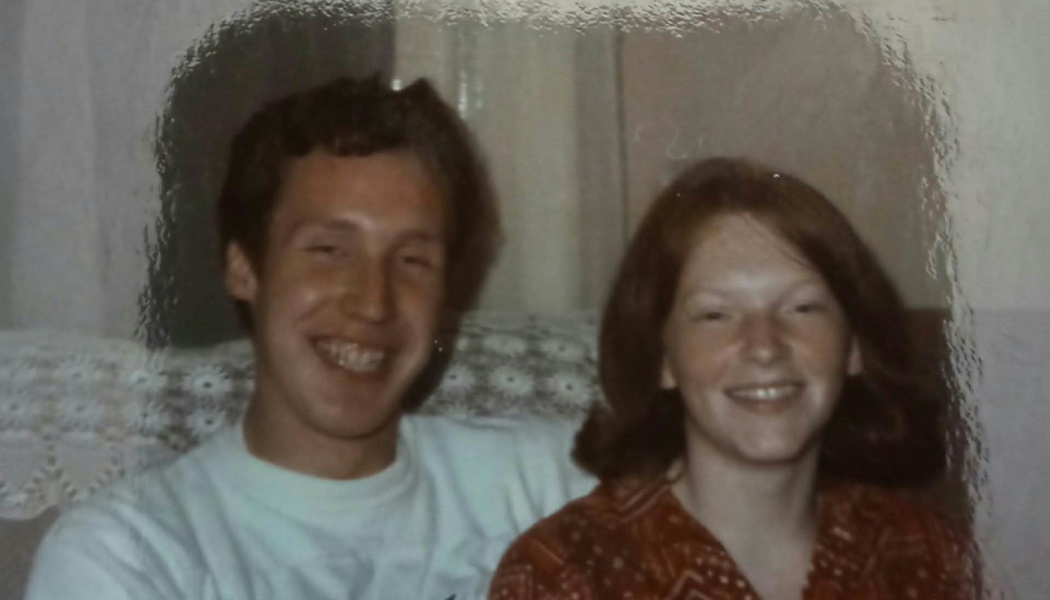 A smiling young couple sitting side by side on a couch in a vintage photograph.
