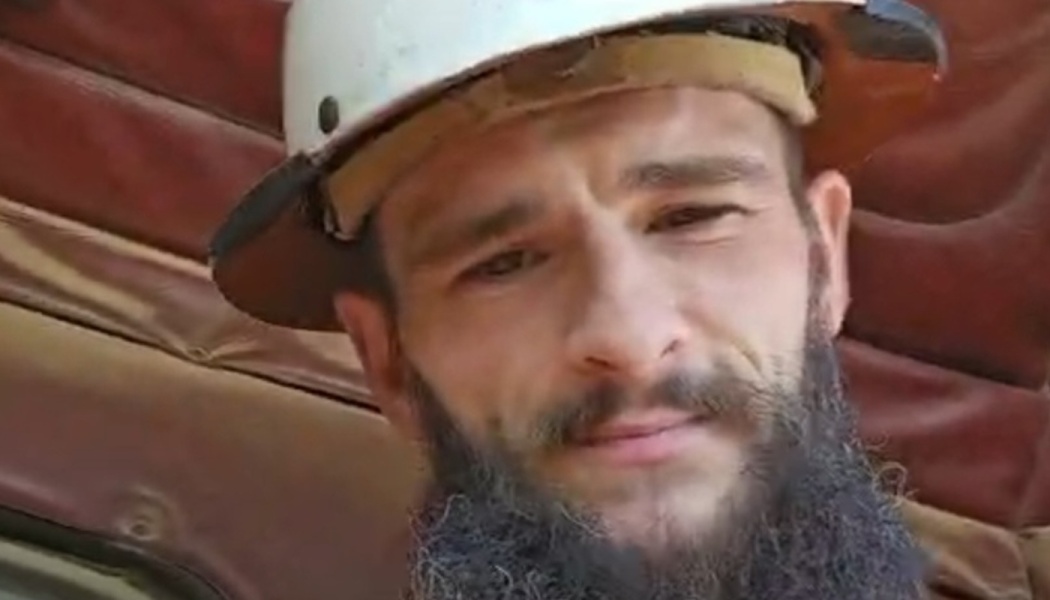 Close-up portrait of a man with a dark beard wearing a white hard hat.