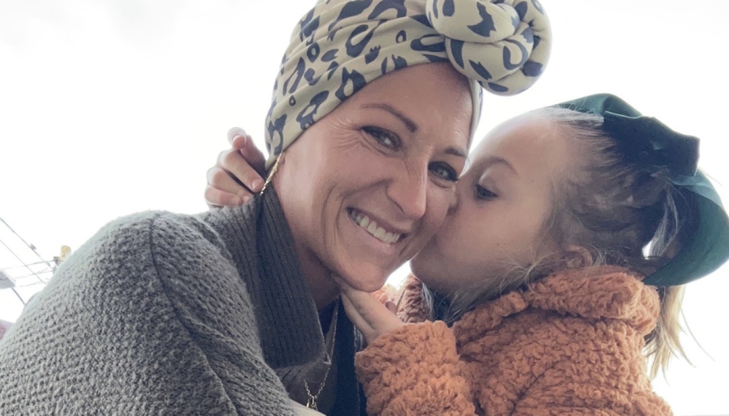 A smiling woman wearing a leopard-print headwrap gets a kiss on the cheek from a young girl.