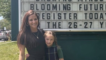 A smiling woman and young girl stand together in front of a school marquee sign reading "Blooming Futures."