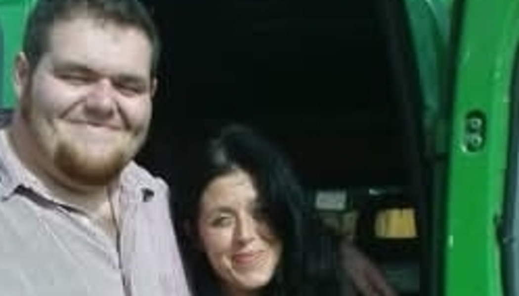 A smiling man and a dark-haired woman standing together in front of a green vehicle.
