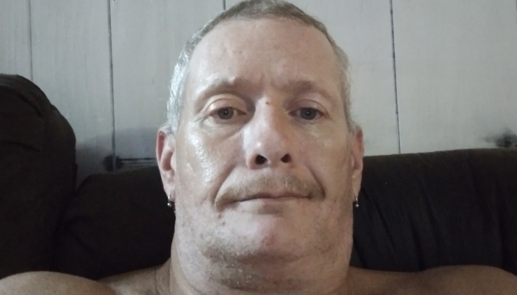A middle-aged man with short gray hair, a mustache, and small earrings looking at the camera.