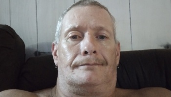 A middle-aged man with short gray hair, a mustache, and small earrings looking at the camera.