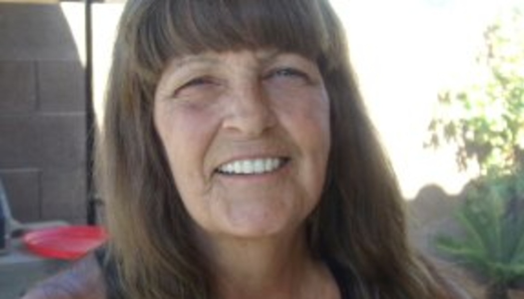 A smiling mature woman with long brown hair and bangs outdoors.
