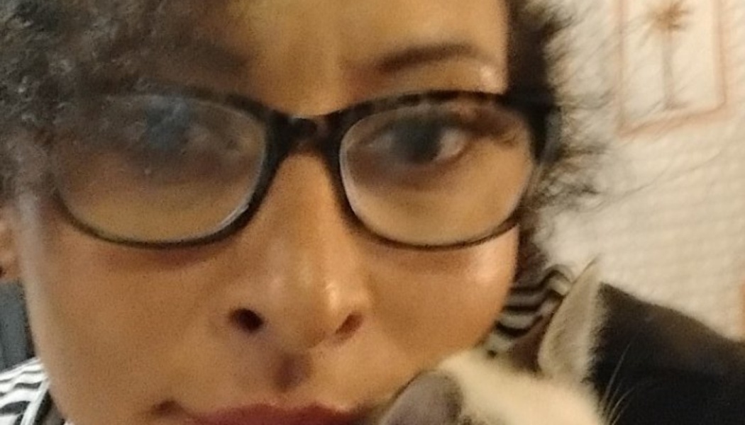 Close-up of a woman wearing glasses cuddling a small grey and white kitten next to her face.