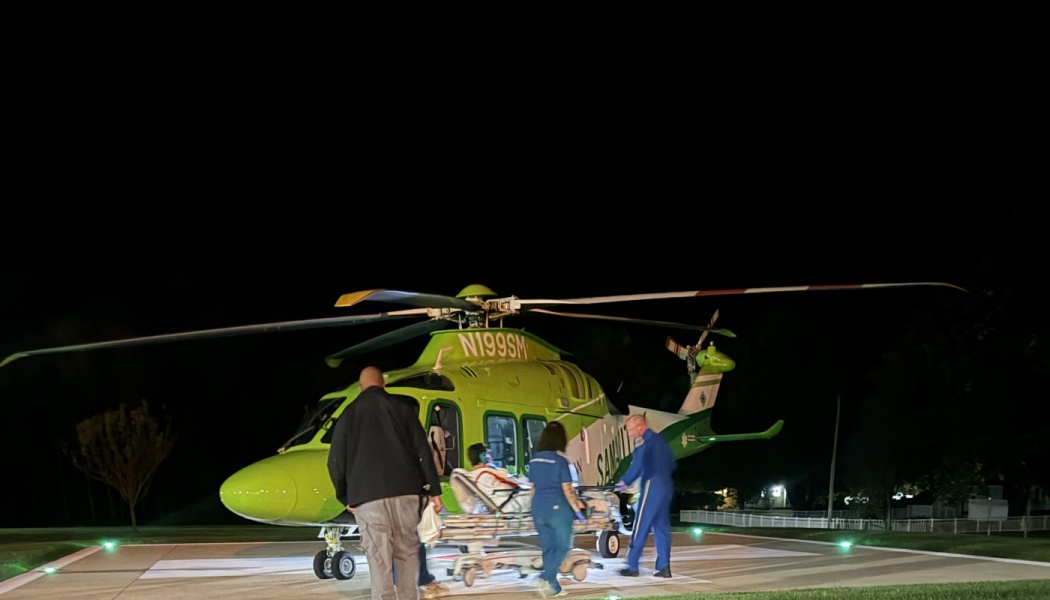 Medical responders loading a patient on a stretcher into a green air ambulance helicopter at night.