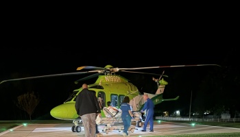 Medical responders loading a patient on a stretcher into a green air ambulance helicopter at night.