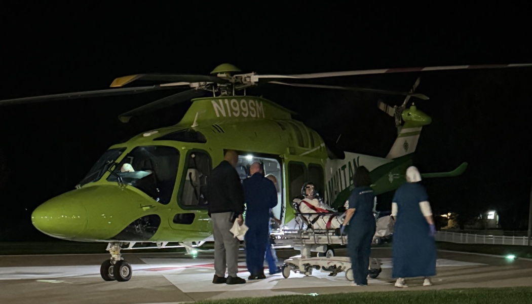 Medical personnel loading a patient on a stretcher into a green medical helicopter on a helipad at night.