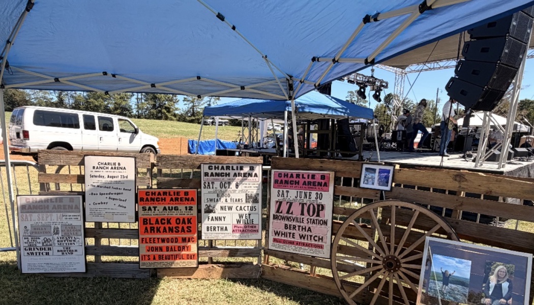 Vintage rock concert posters and a wooden wagon wheel displayed on pallets beneath a blue canopy tent.
