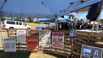 Vintage rock concert posters and a wooden wagon wheel displayed on pallets beneath a blue canopy tent.