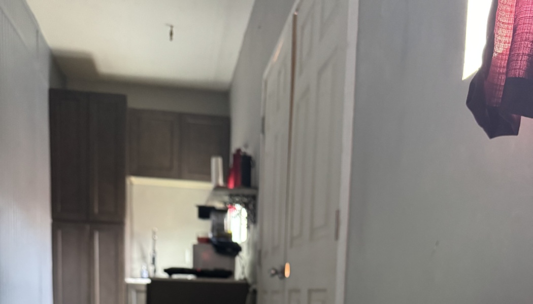 Blurry view looking down a narrow hallway toward a small kitchen with dark brown cabinets.