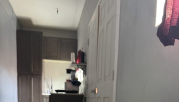 Blurry view looking down a narrow hallway toward a small kitchen with dark brown cabinets.