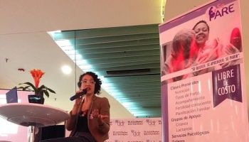 A woman speaking into a microphone next to a banner advertising free prenatal classes.