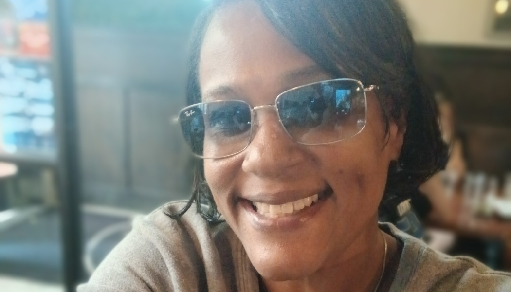 A smiling woman with short dark hair wearing silver-framed sunglasses.