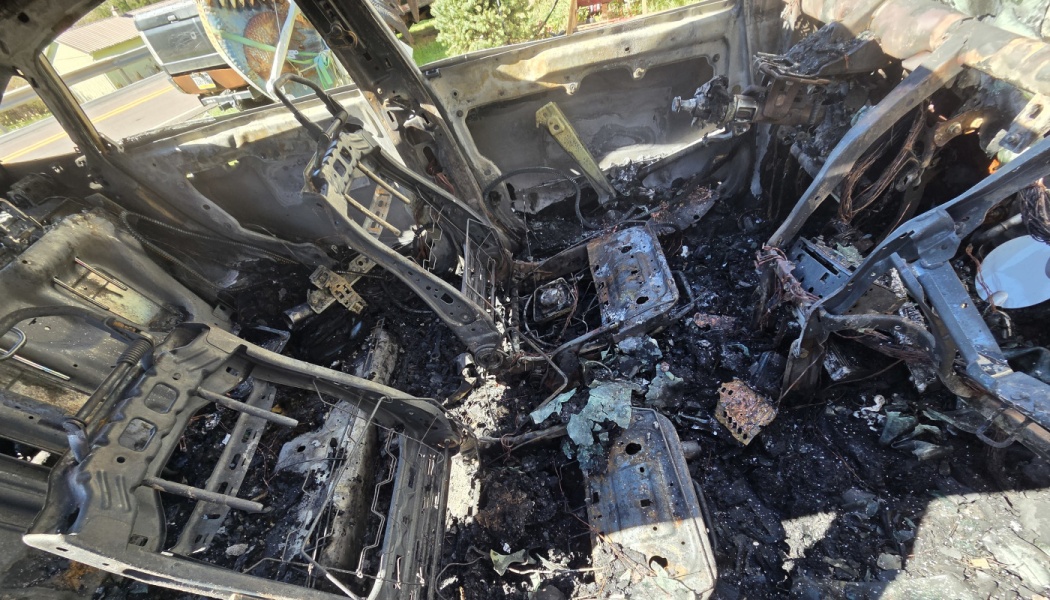 Severely burned interior of a car, reduced to charred metal seat frames, ash, and exposed wires.