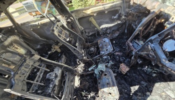 Severely burned interior of a car, reduced to charred metal seat frames, ash, and exposed wires.