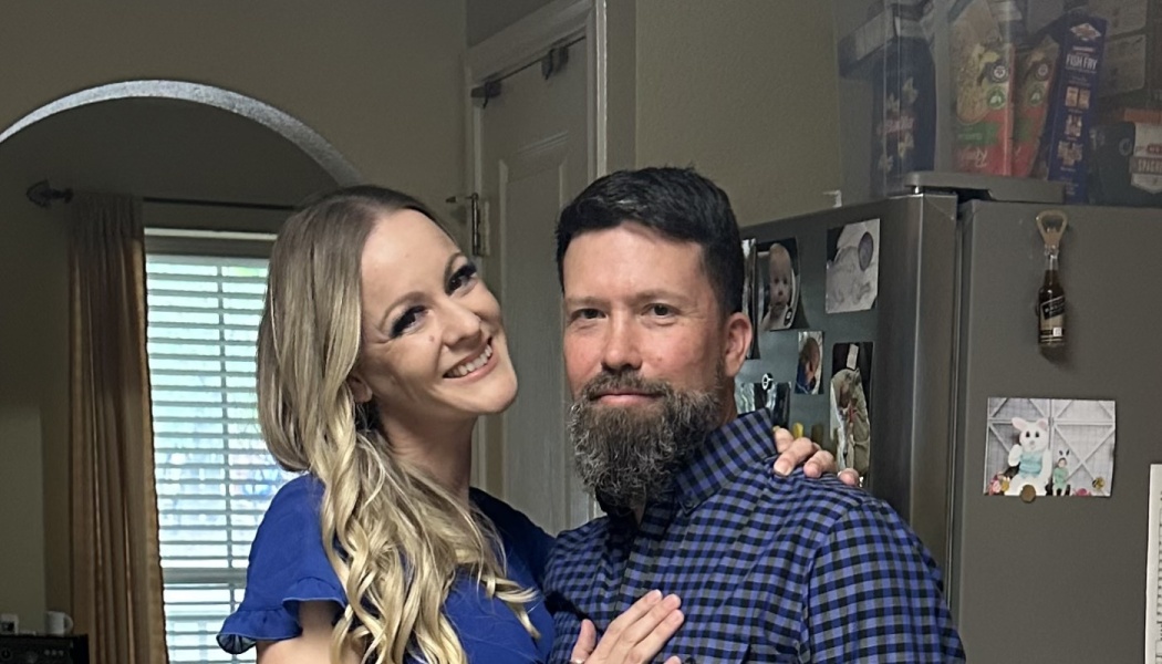 A smiling blonde woman in blue posing affectionately next to a bearded man in a blue plaid shirt.