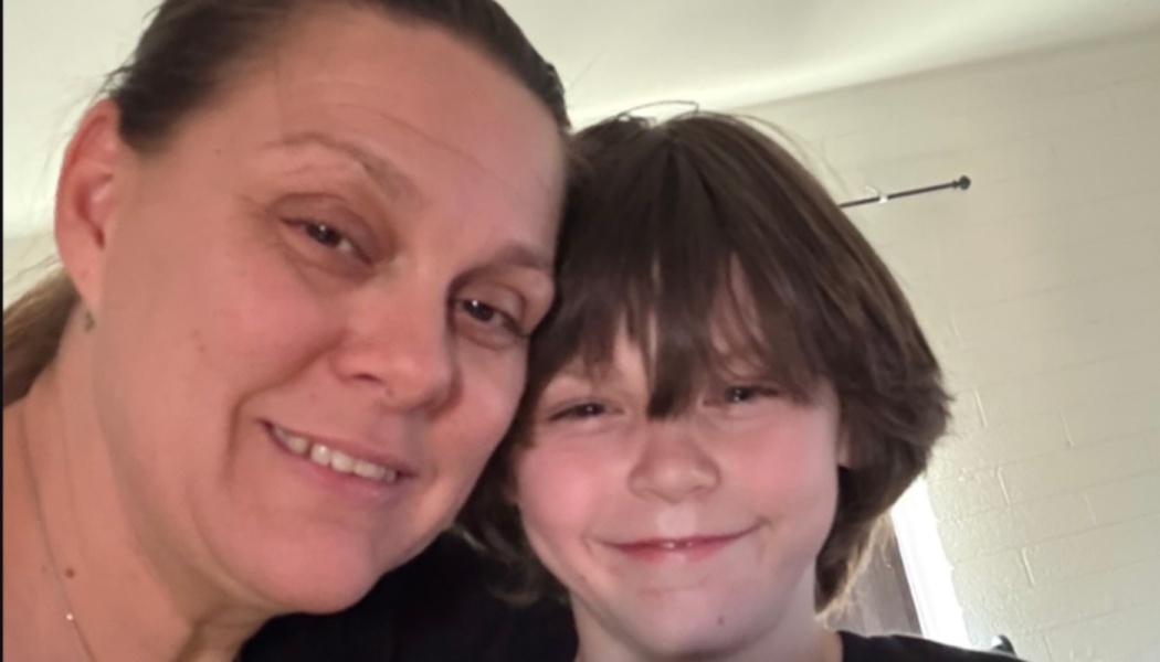 A woman and a young boy smiling warmly with their heads pressed together.