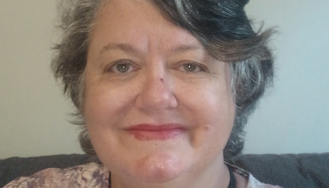 Close-up portrait of a smiling woman with short, wavy salt-and-pepper hair looking at the camera.