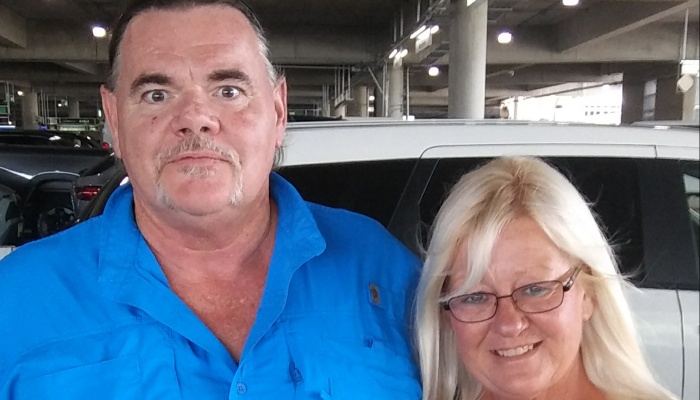 A man in a bright blue shirt stands next to a smiling blonde woman wearing glasses.