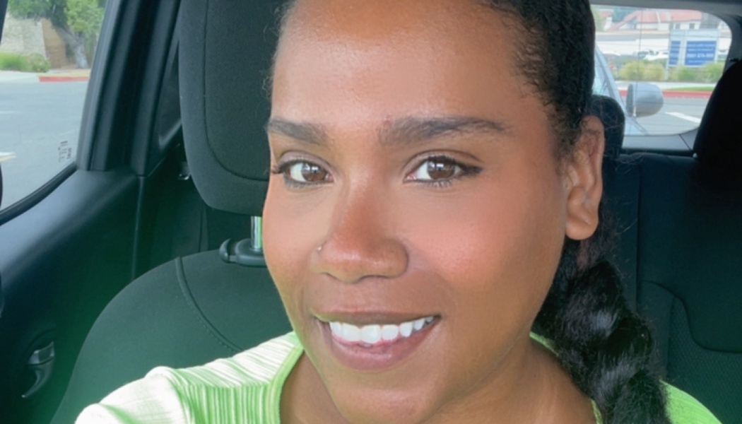 A smiling Black woman with dark braided hair and a lime green top sitting inside a car.