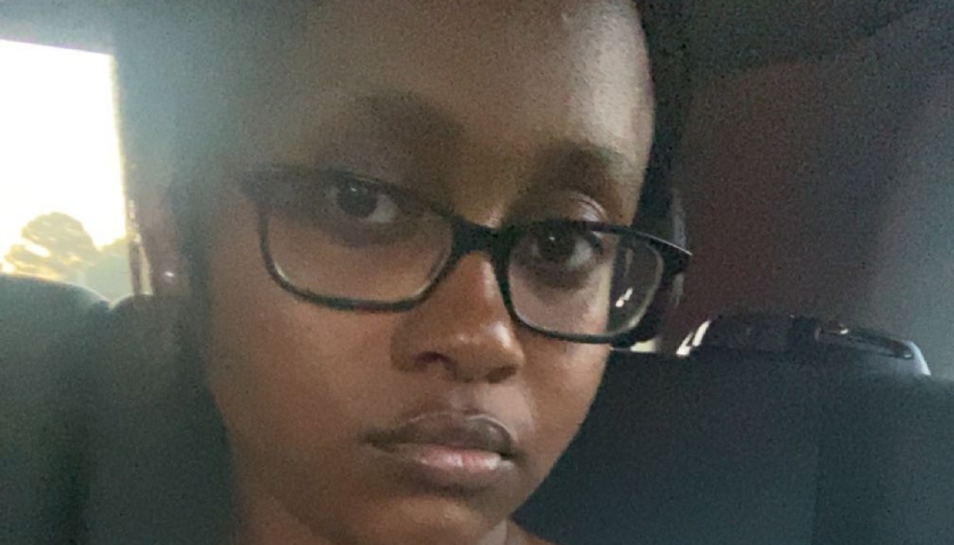 Close-up portrait of a young Black woman with dark-rimmed glasses looking at the camera inside a car.