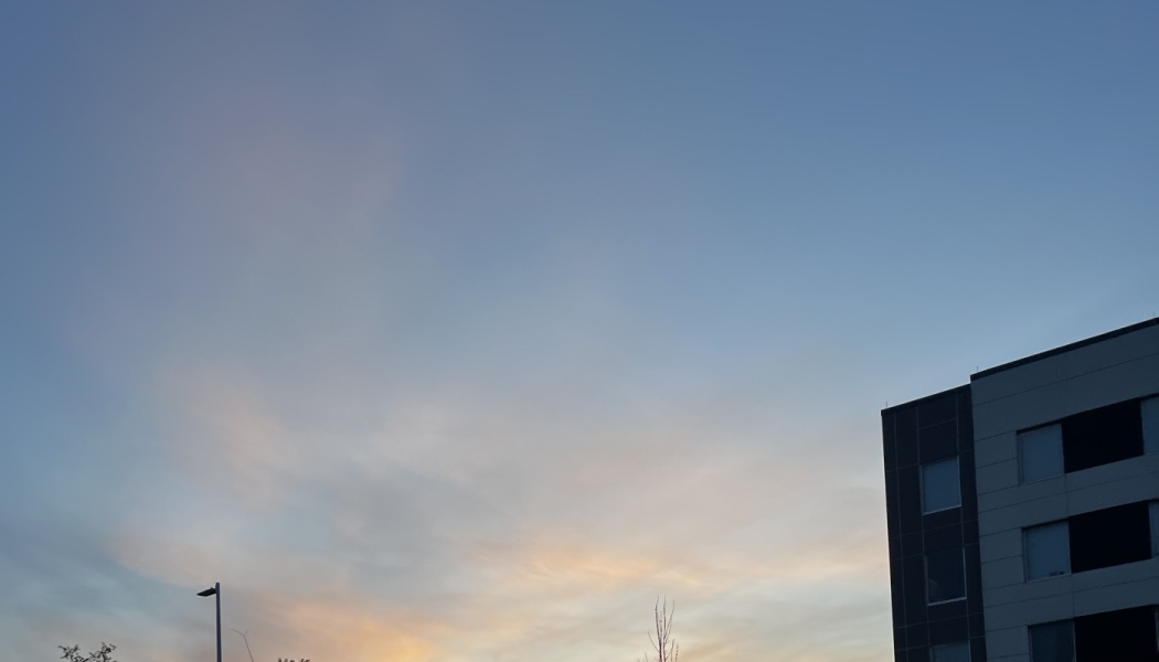 Corner of a modern building set against a wide blue sky with soft sunset colors near the horizon.