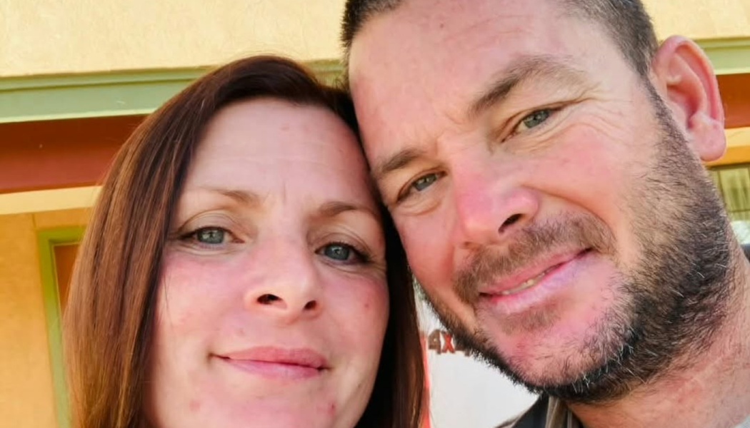 Close-up selfie of a smiling woman with brown hair and a bearded man leaning their heads together.