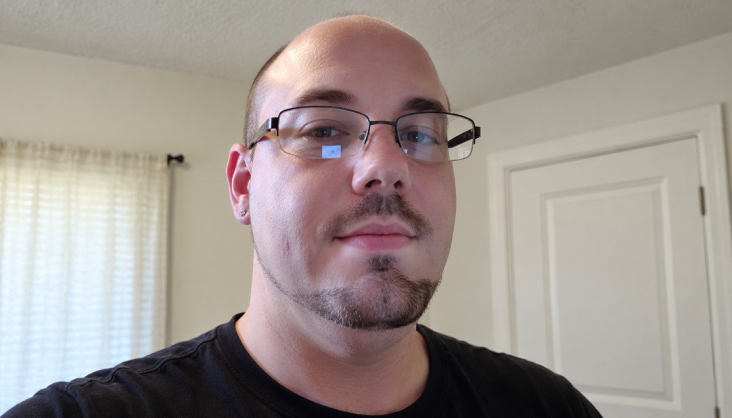 A bald man with glasses and a trimmed goatee, wearing a black t-shirt.