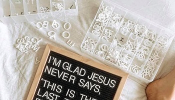A felt letter board reading "I'M GLAD JESUS NEVER SAYS" next to plastic organizers filled with white letters.