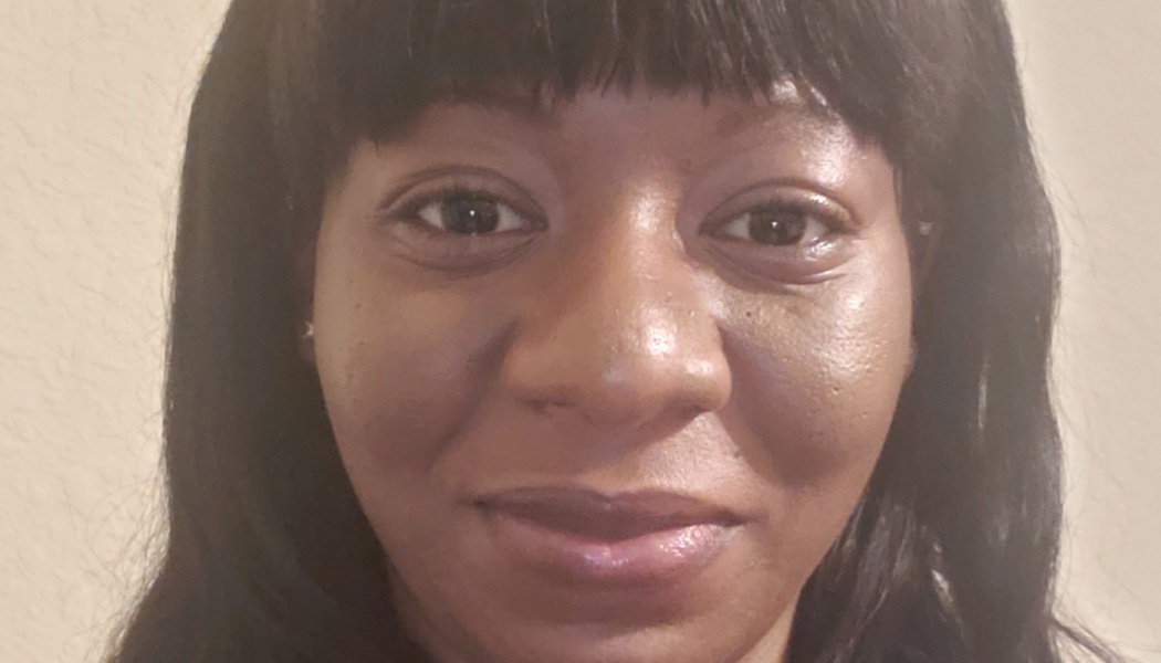 Close-up portrait of a Black woman with dark hair and bangs, looking at the camera with a subtle smile.