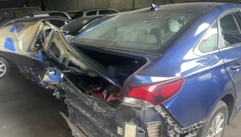 Blue sedan with severe rear-end collision damage, showing a heavily crushed trunk and destroyed back bumper.