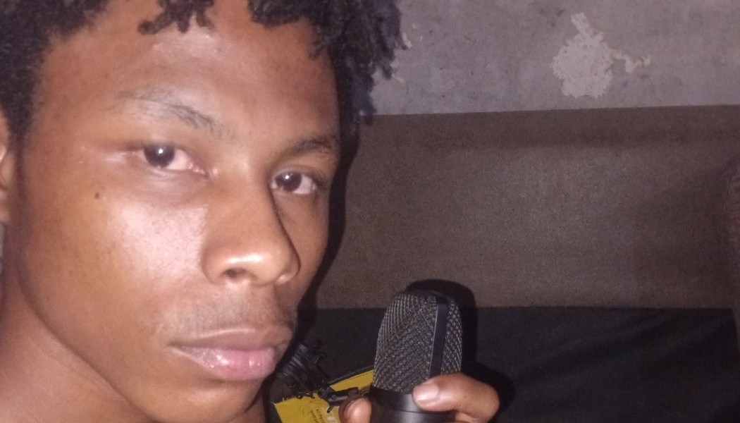 A young Black man looking directly at the camera while holding a studio microphone.