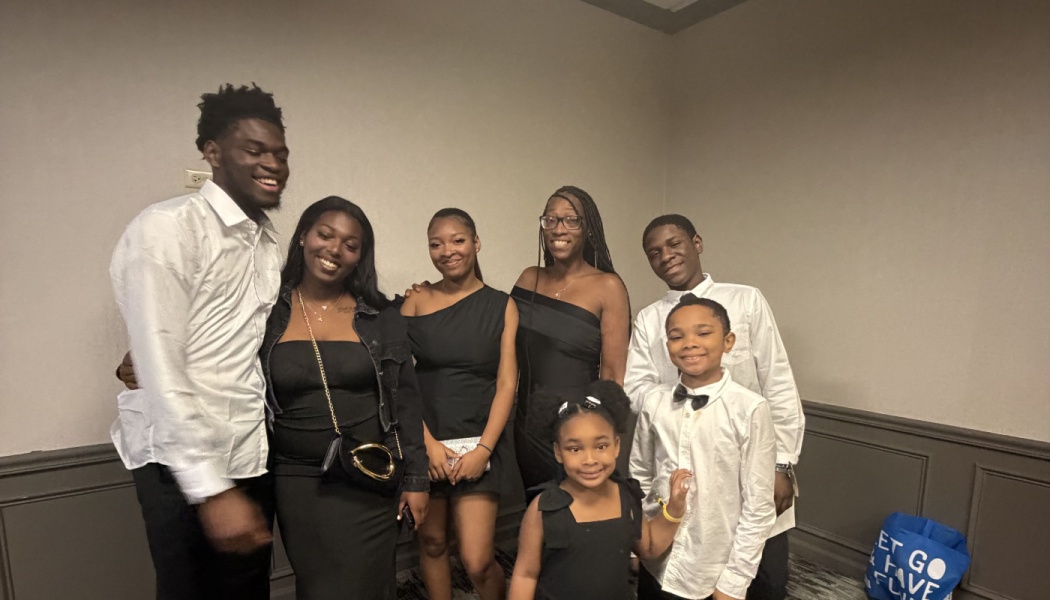 A smiling Black family dressed in black and white formal attire posing together indoors.