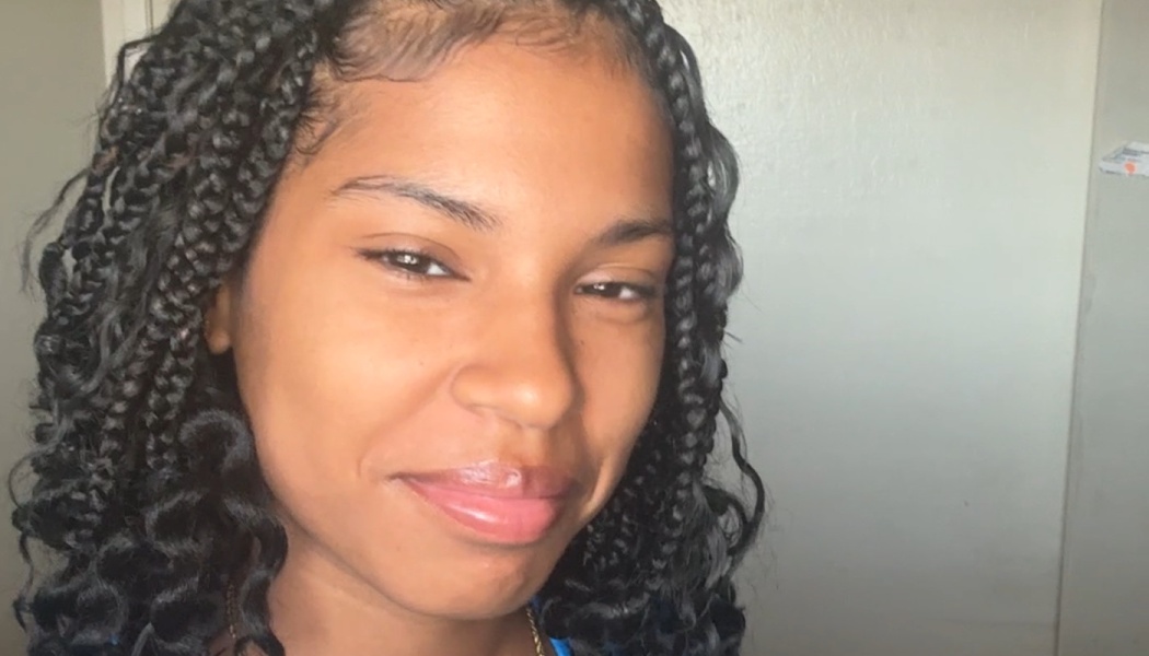 Young woman with dark braided hair smiling gently at the camera.