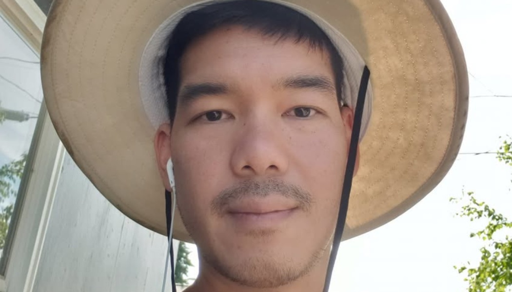 Close-up portrait of a man wearing a wide-brimmed sun hat and white earphones outdoors.