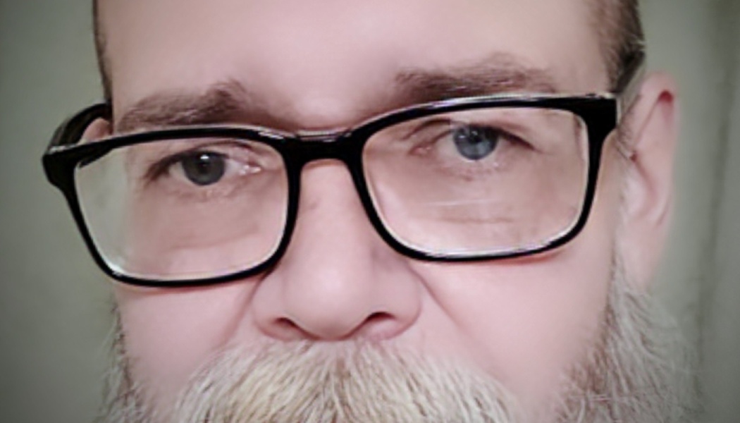Close-up portrait of a man wearing black-framed glasses and a grey beard.
